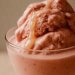Sorvete de morango com iogurte cremoso servido em taça de vidro, com mel escorrendo suavemente sobre o topo.