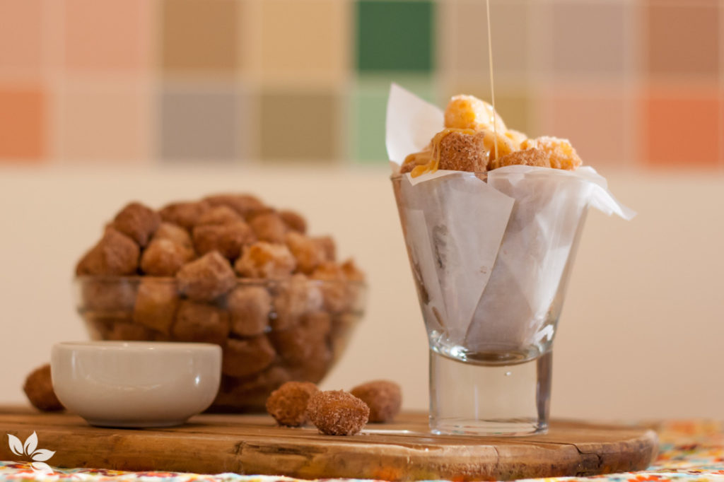 Receita de churros simples servidos em copo de vidro com açúcar e canela.