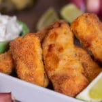 Porção de isca de tilápia empanada e dourada, servida com molho tártaro e limão.