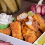 Porção de isca de tilápia empanada e dourada, servida com molho tártaro e limão.